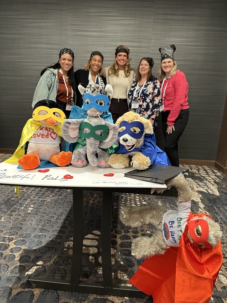 Catalyst employees posing behind a table with handmade stuffed animals in super hero costumes.